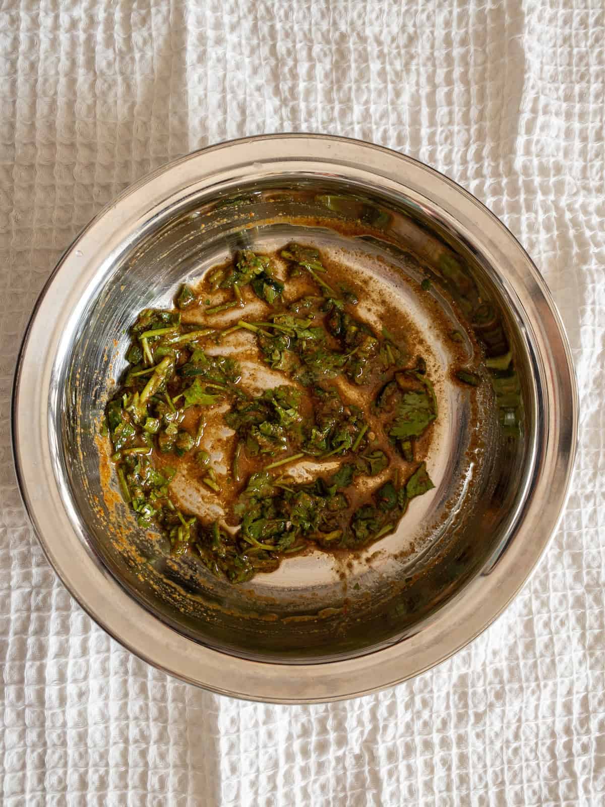 Mixed lemon dressing with chopped coriander and spices in a stainless steel bowl.
