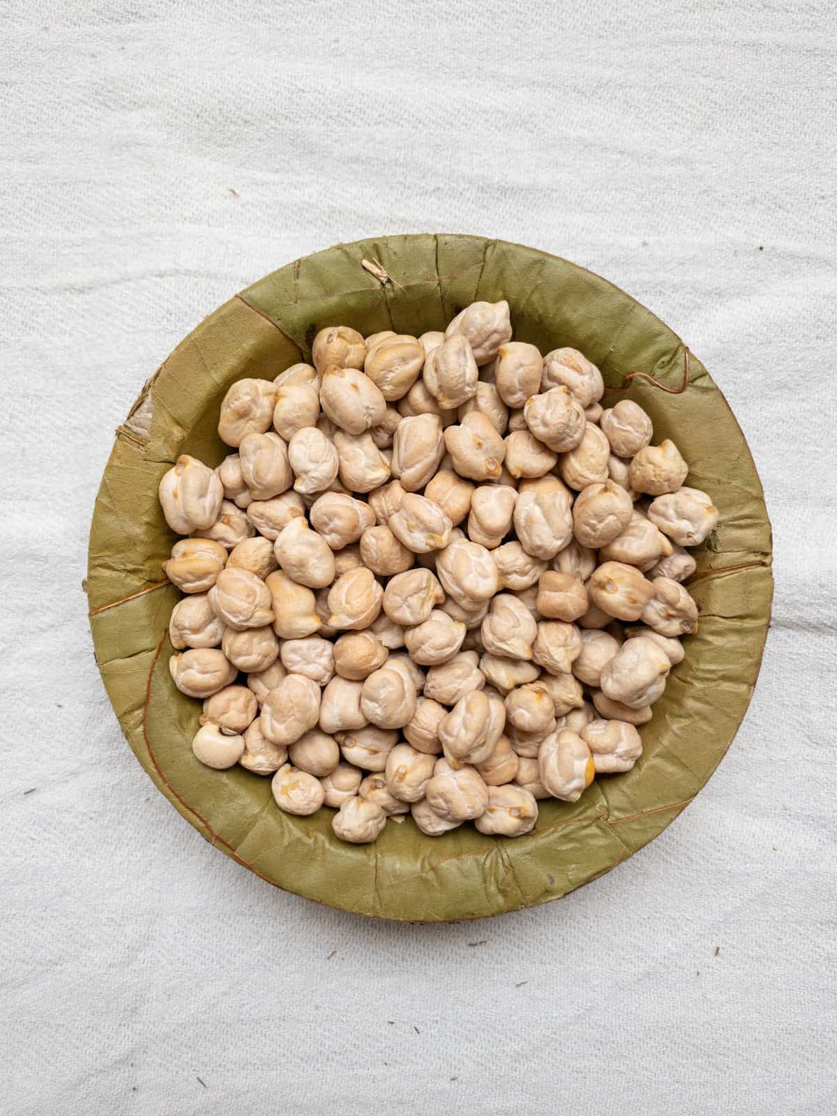 Chickpeas in a leaf bowl on a white cloth.
