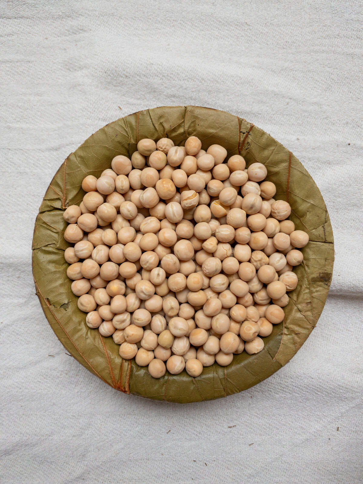 Dried yellow peas in a leaf bowl on a white cloth.