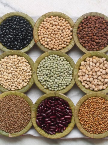 Different dried beans and legumes arranged in leaf bowls.