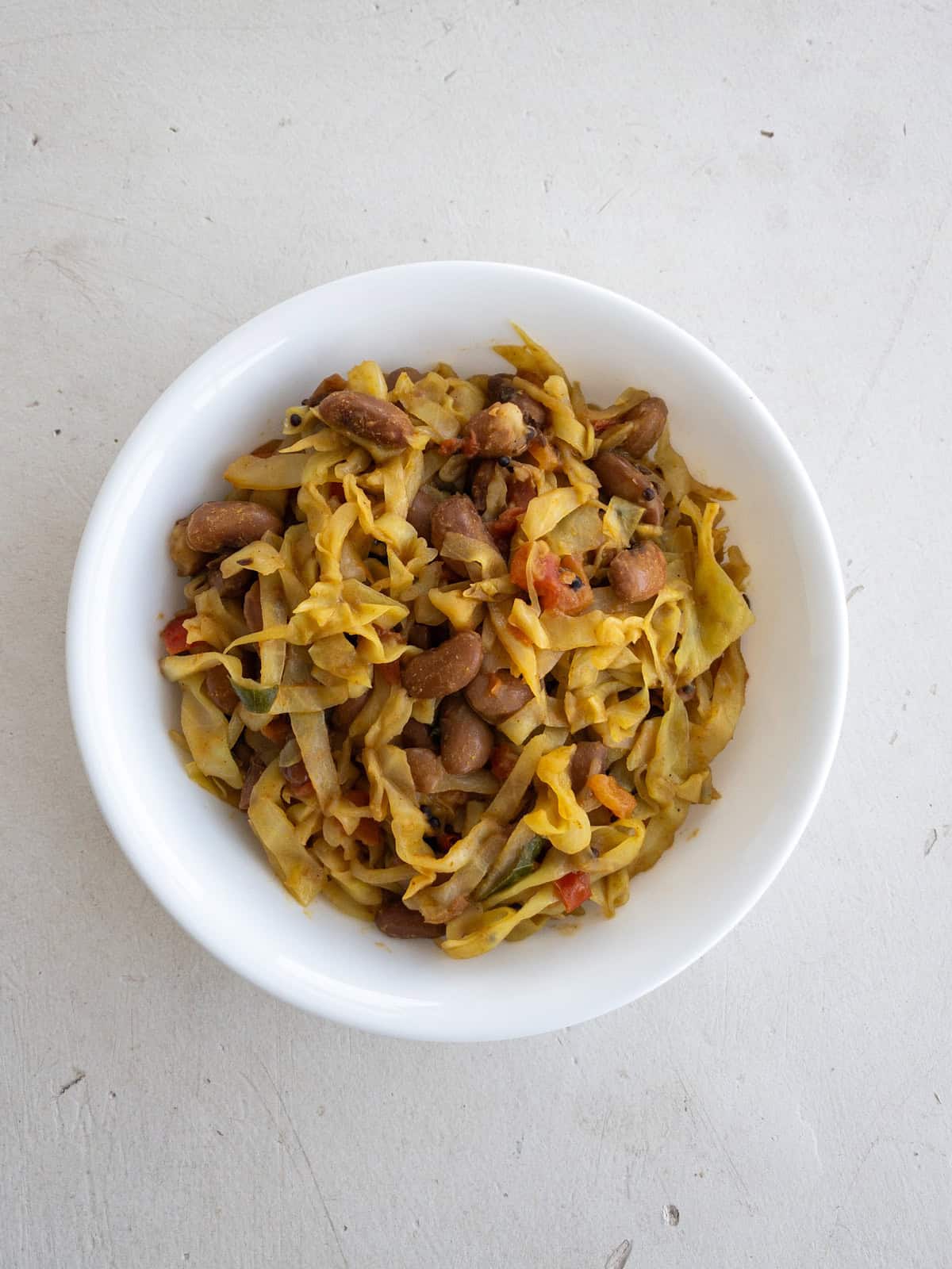 Bowl of Indian cabbage stir fry with kidney beans on a light surface.