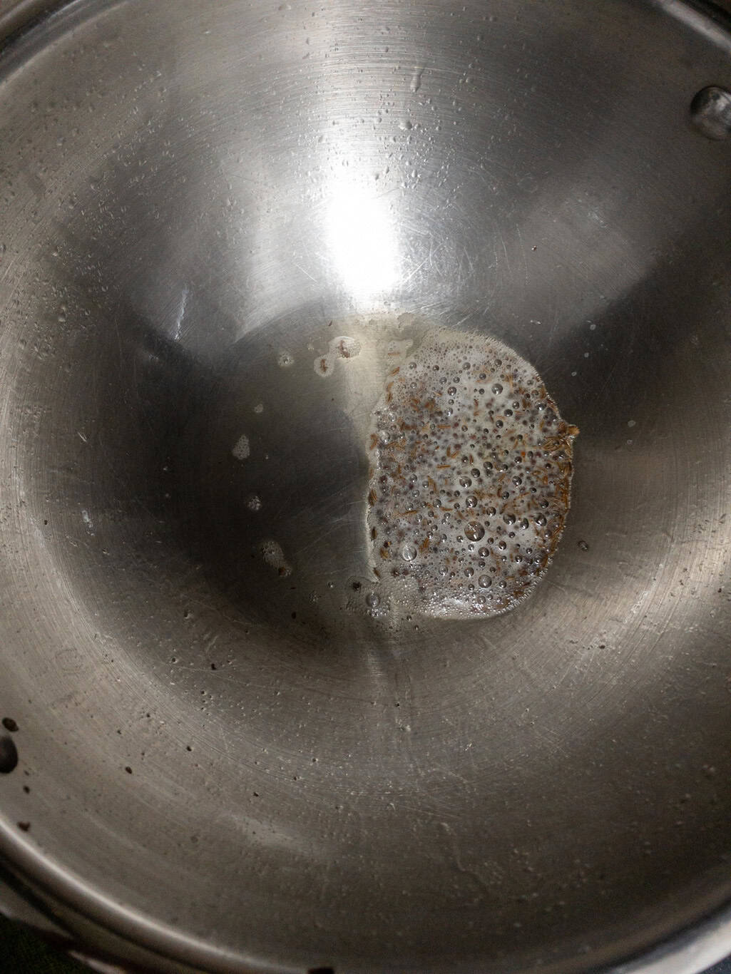 Mustard seeds and cumin seeds sizzling in hot oil in a steel pan.