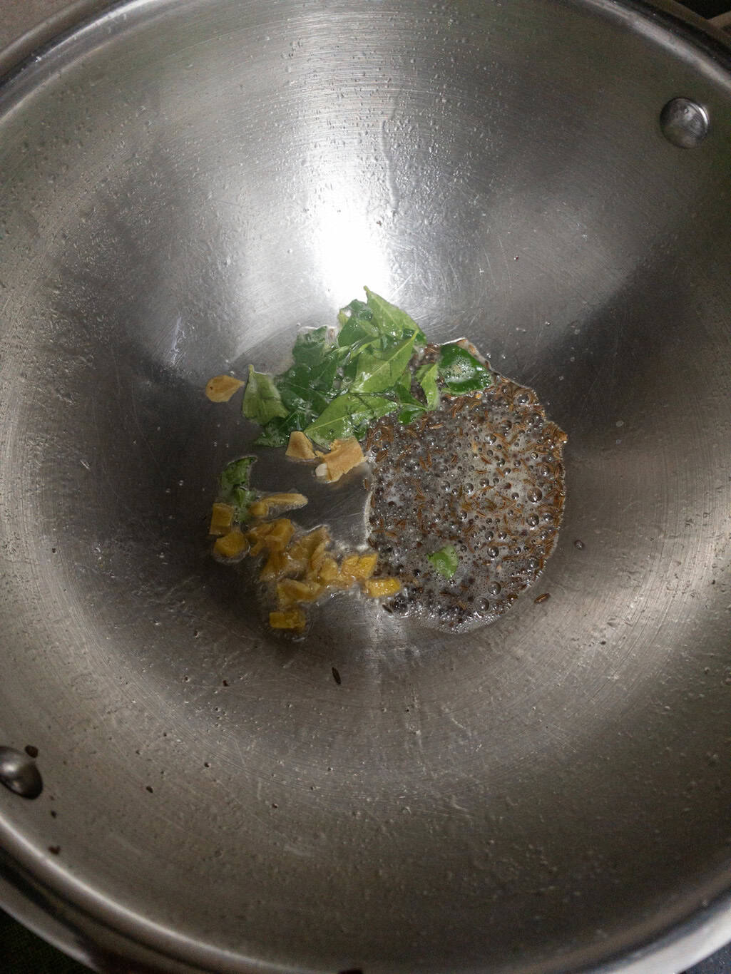 Curry leaves and chopped ginger added to sizzling tempered spices in a pan.