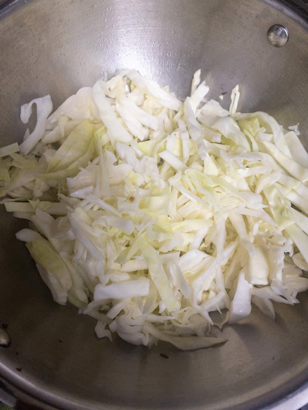 Fresh shredded cabbage added to a steel pan for stir frying.