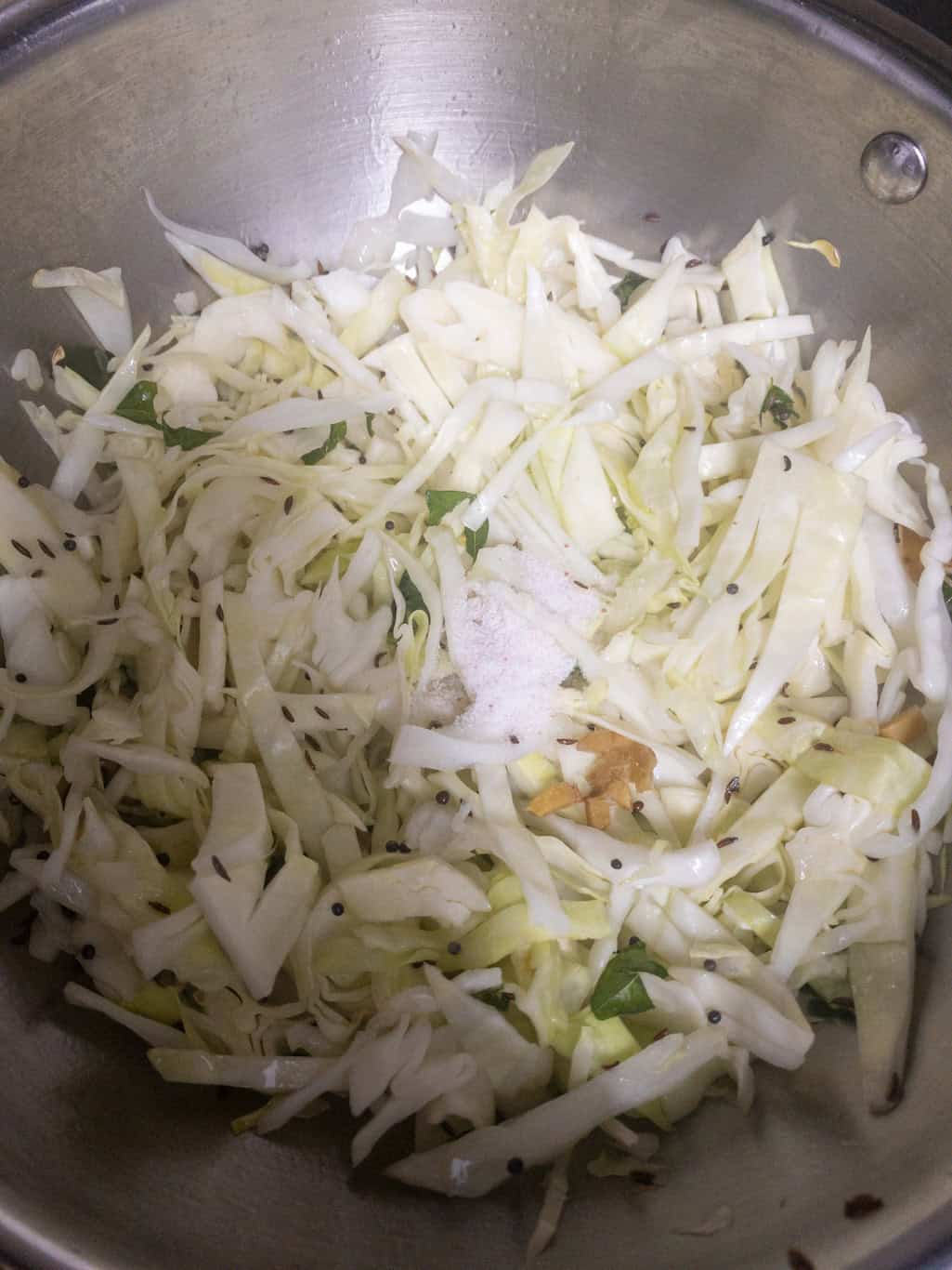Salt added over shredded cabbage and tempered spices in a pan.