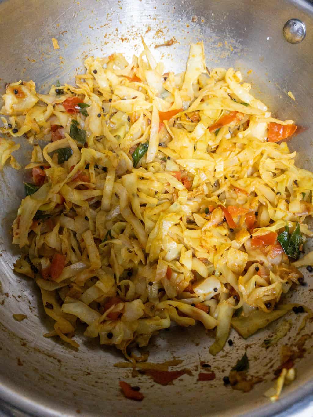 Cabbage cooked with tomatoes, curry leaves, and spices in a steel pan.