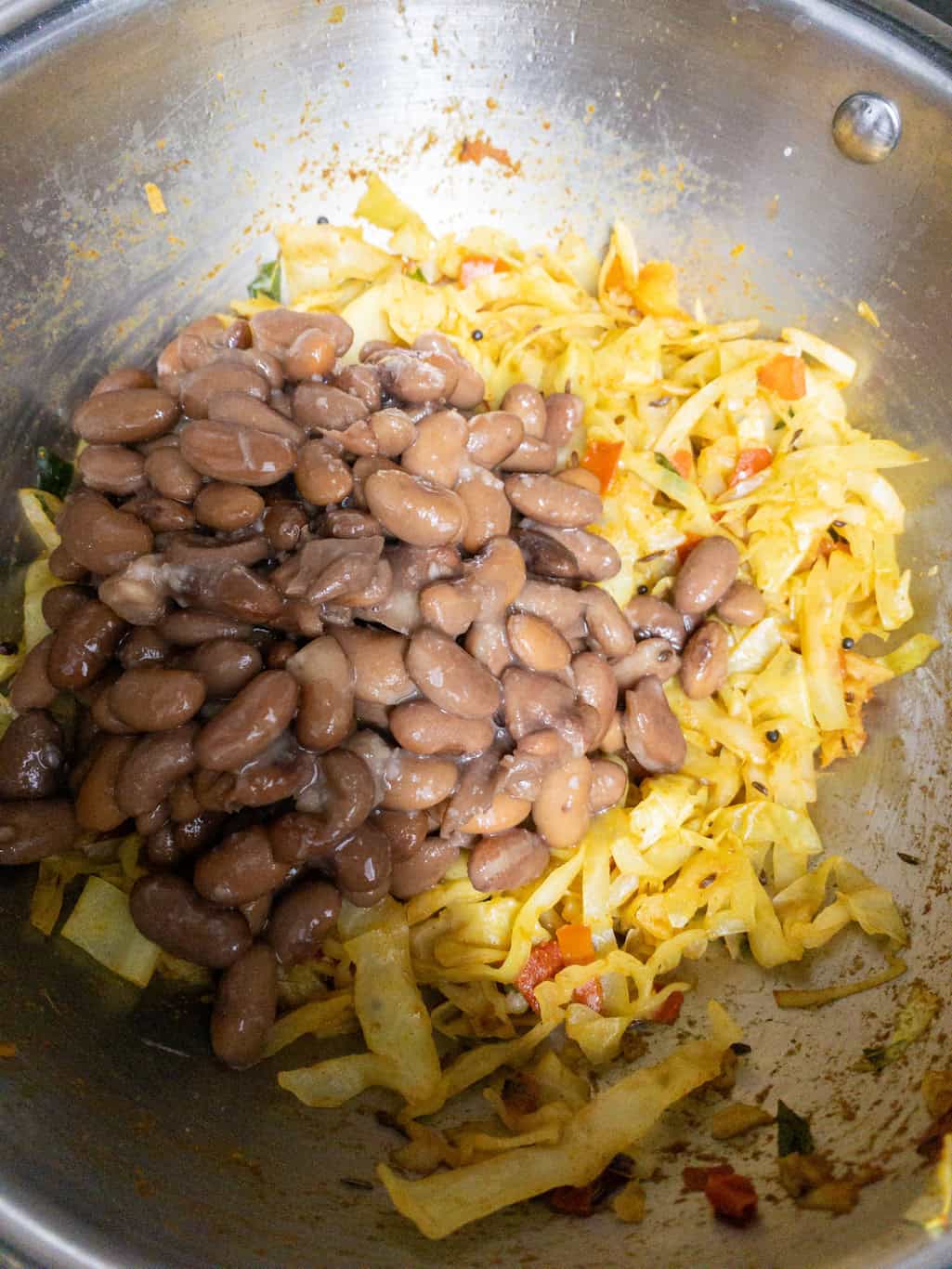 Cooked kidney beans added to spiced cabbage in a steel pan.