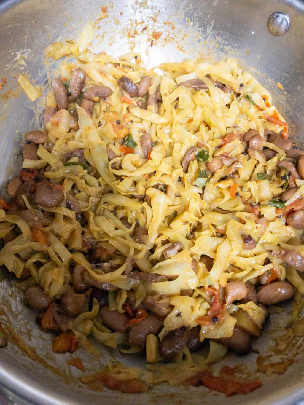Finished cabbage and kidney bean stir fry mixed together in a steel pan.