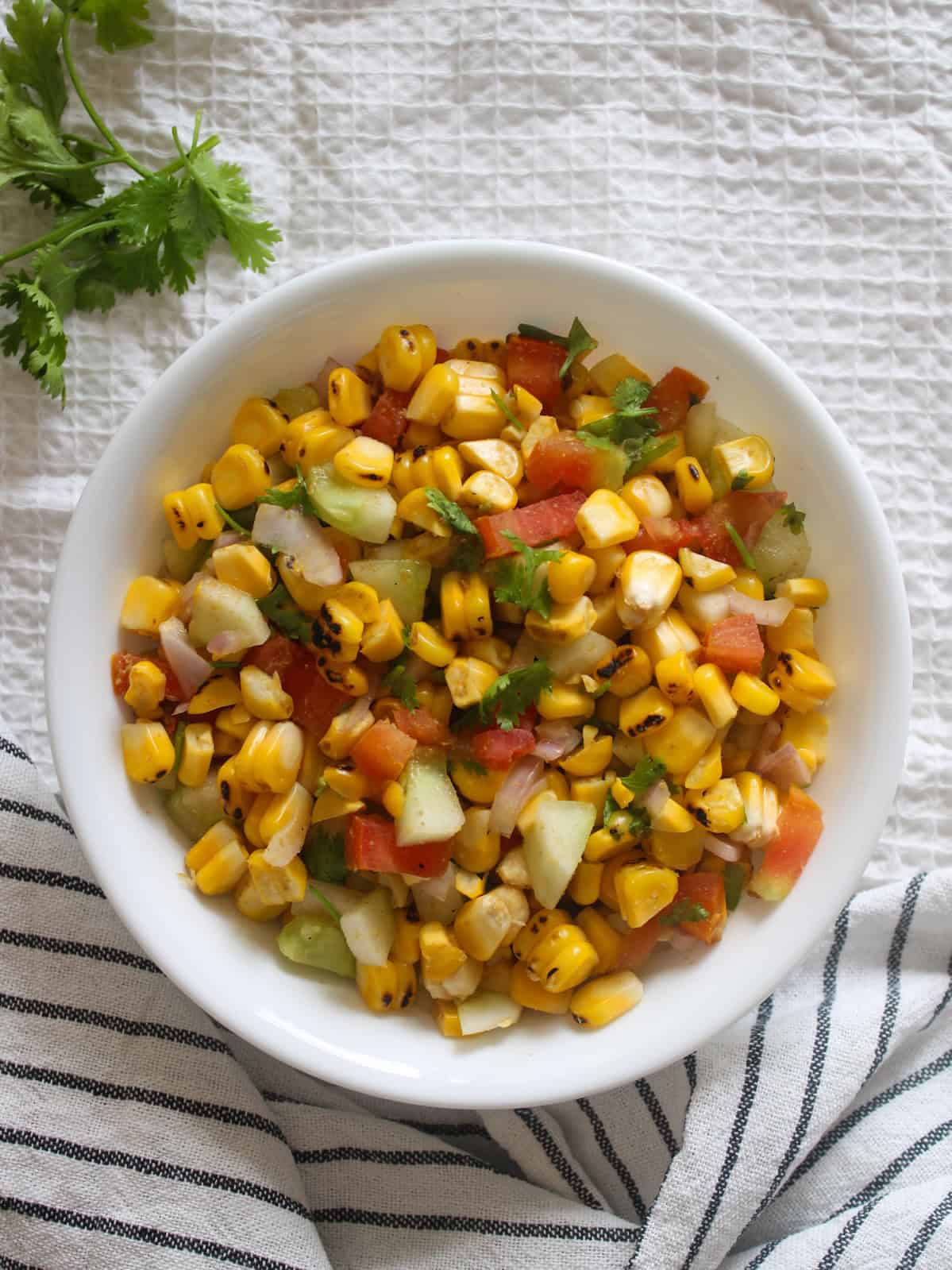 Colorful grilled corn salad with charred kernels, cucumber, tomato, onion, and fresh coriander.