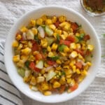 Close view of grilled corn salad with crisp vegetables and coriander in a white serving bowl.
