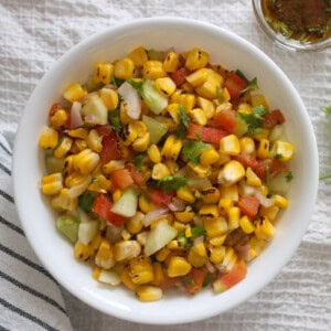 Close view of grilled corn salad with crisp vegetables and coriander in a white serving bowl.