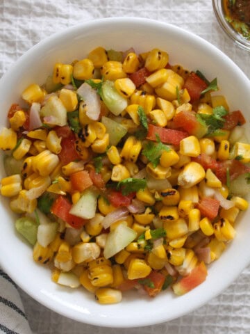 Close view of grilled corn salad with crisp vegetables and coriander in a white serving bowl.