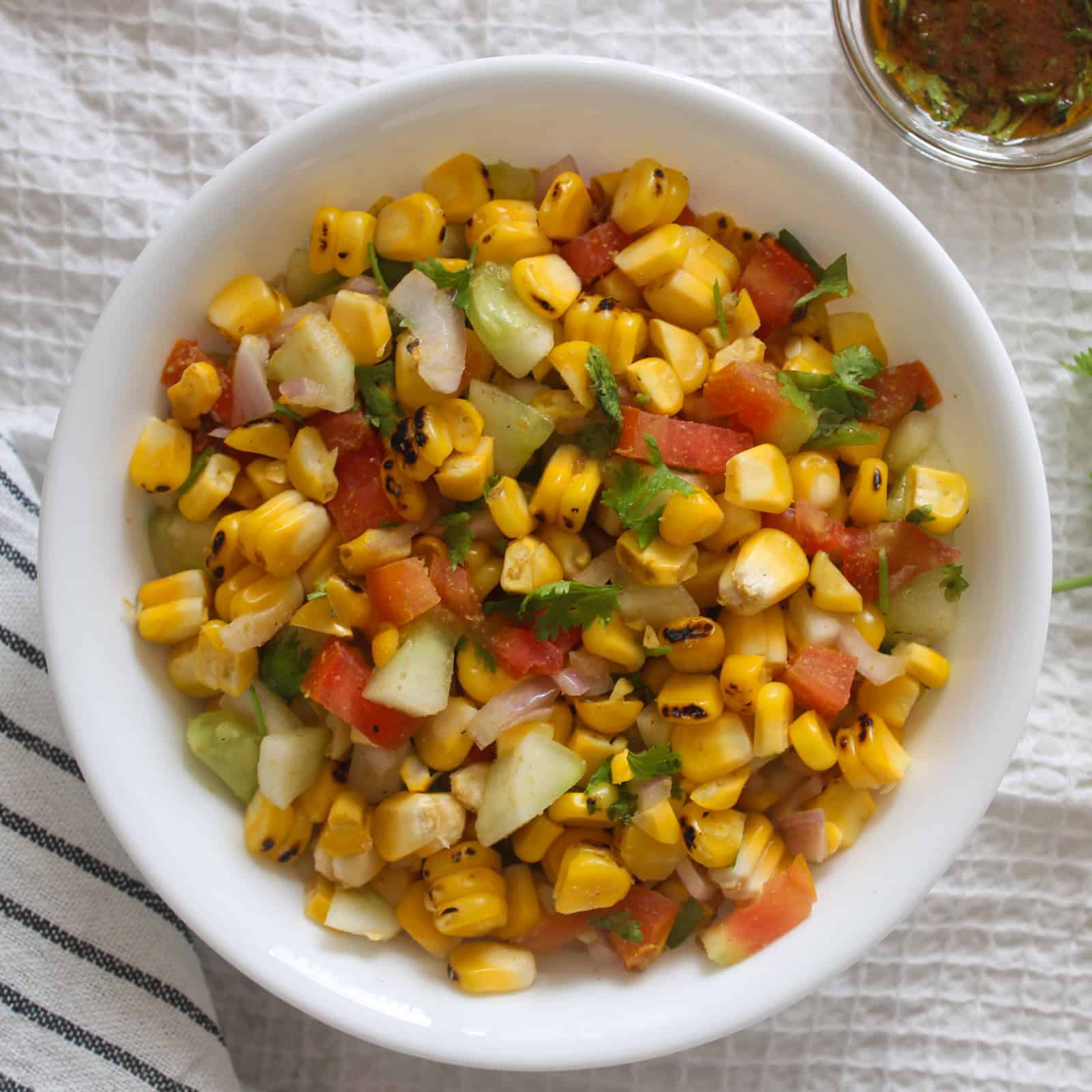 Close view of grilled corn salad with crisp vegetables and coriander in a white serving bowl.