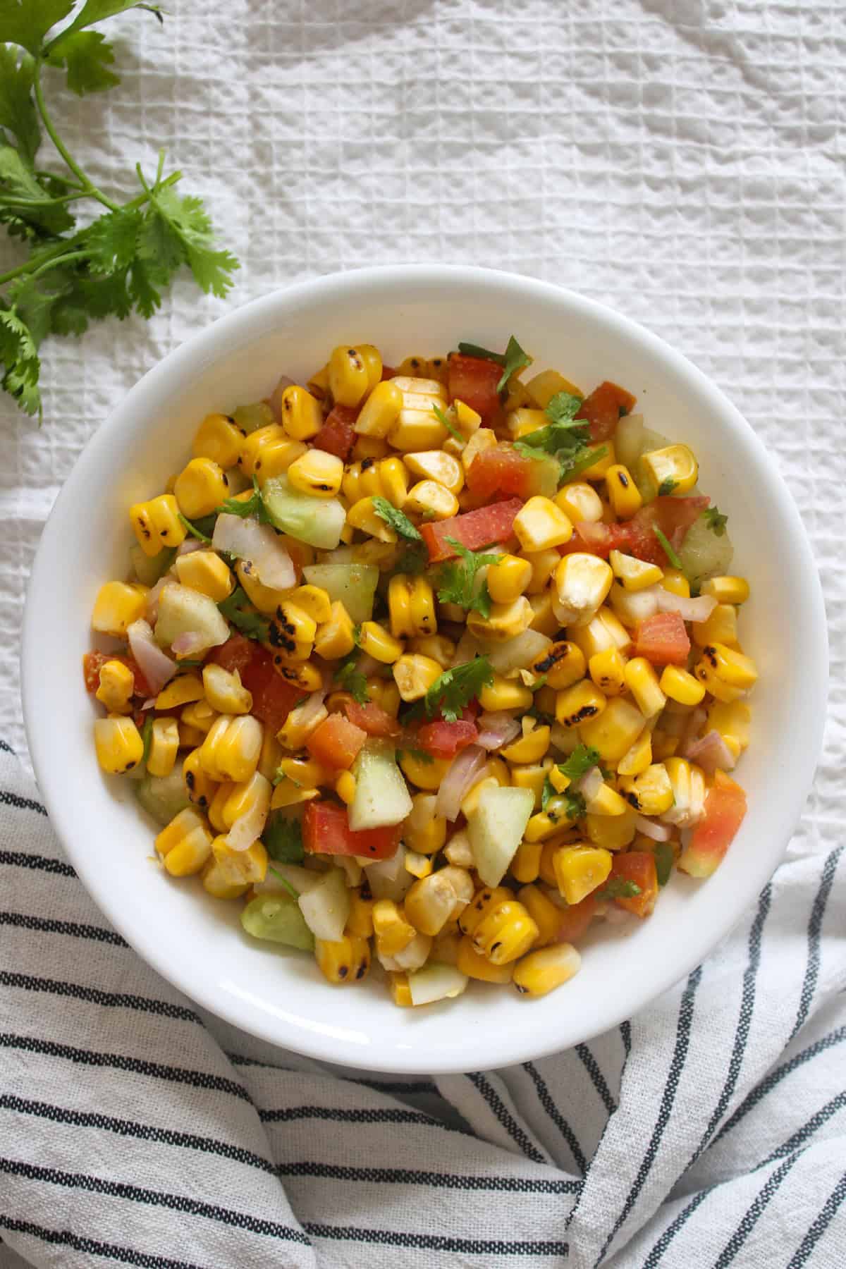 Indian chaat-style grilled corn salad with cucumber, tomato, onion, and coriander served in a white bowl.