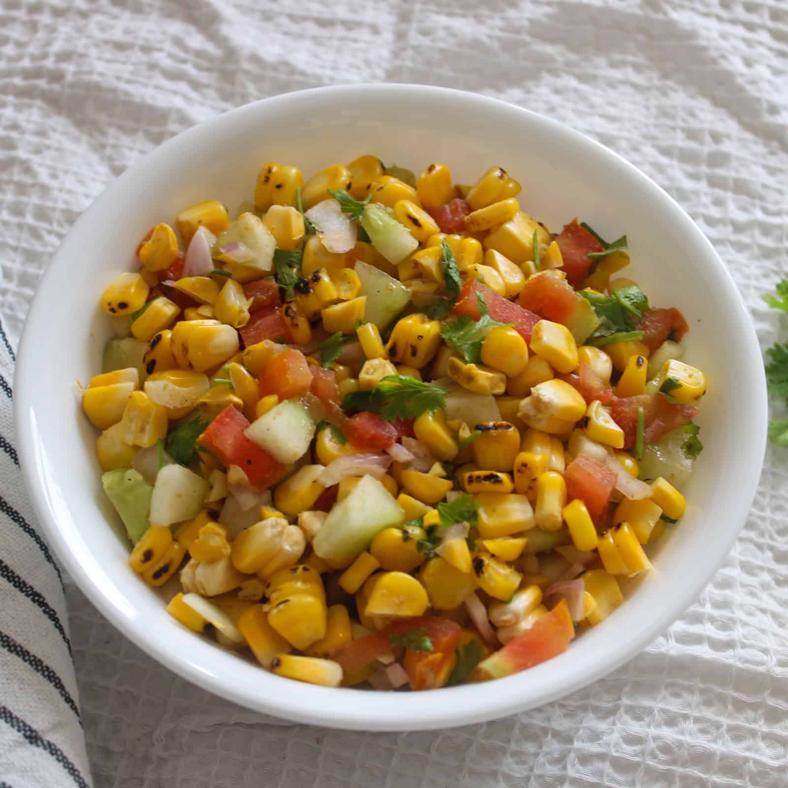 Chaat-style grilled corn salad served in a white bowl with visible charred corn and chopped vegetables.