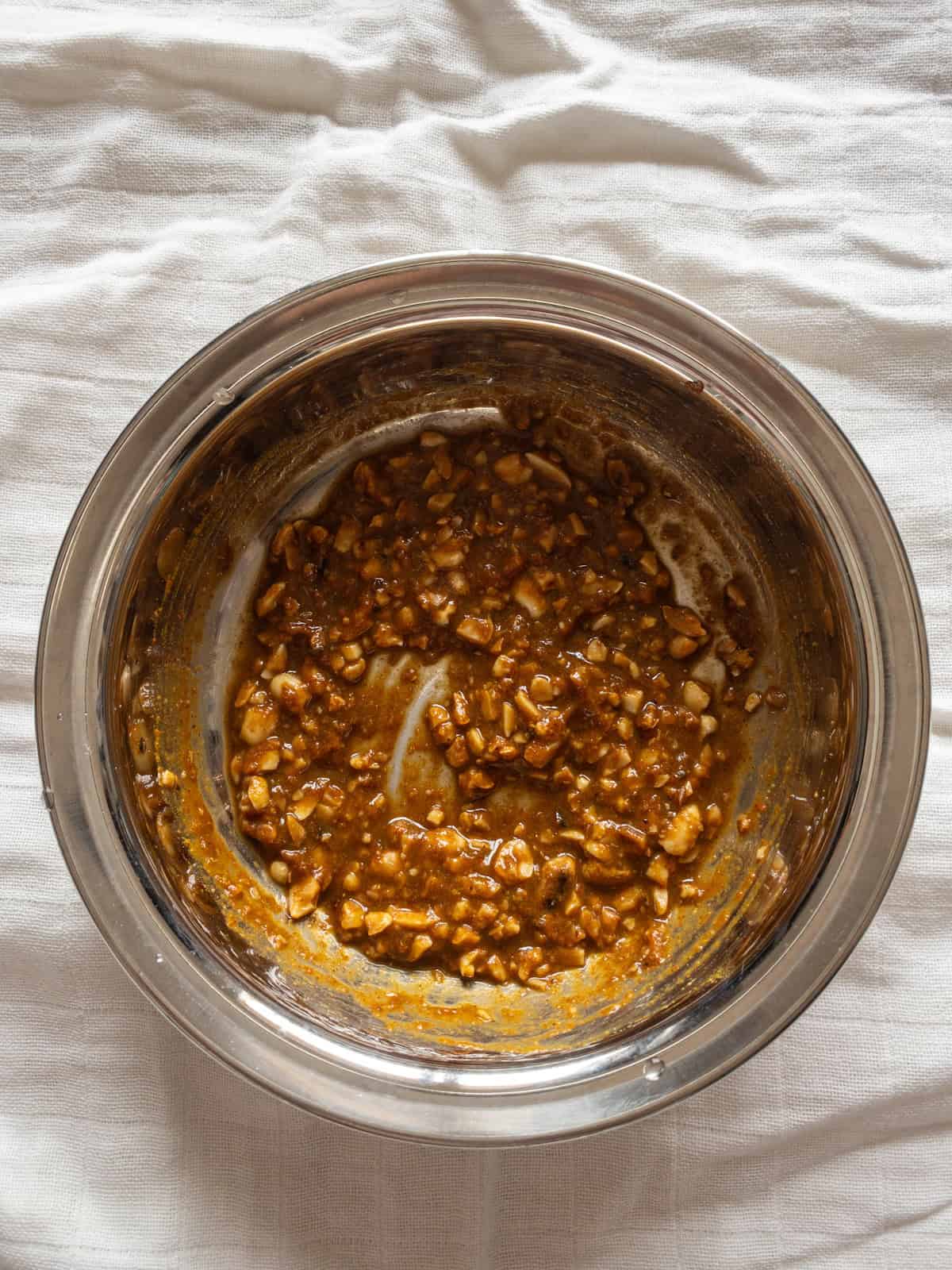Thick tamarind peanut dressing mixed with crushed peanuts and spices in a stainless steel bowl.