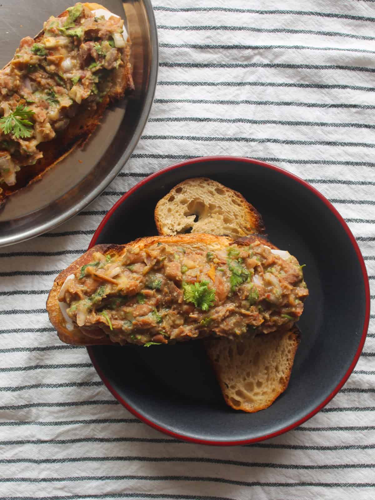 Toasted bread topped with mashed kidney beans served in a black bowl with extra toast nearby.