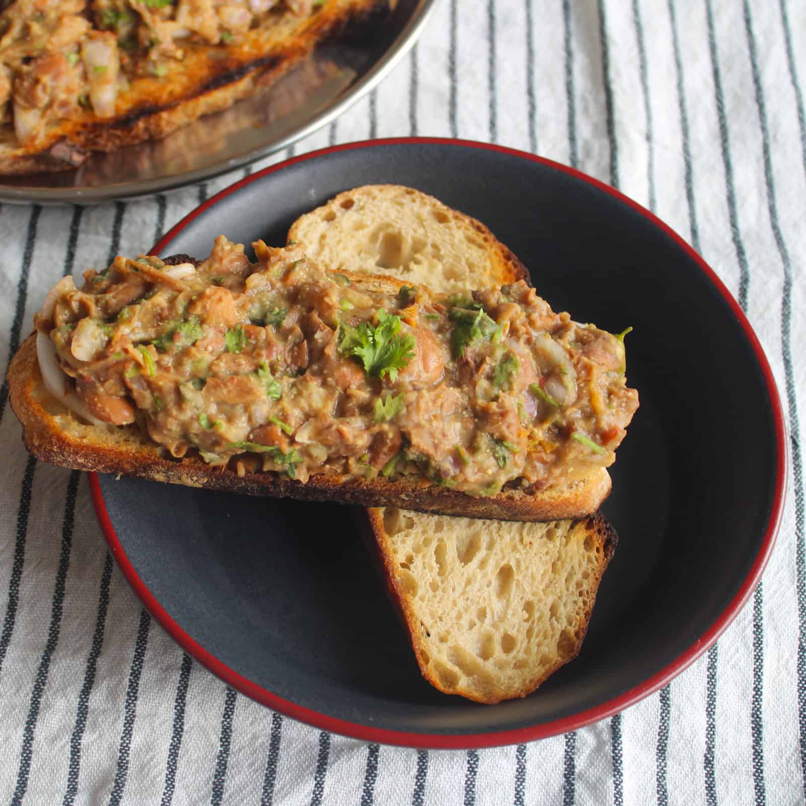 Close view of kidney bean mash spread over cucumber and toasted bread in a black bowl.