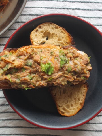 Mashed kidney bean toast with cucumber served in a black bowl.
