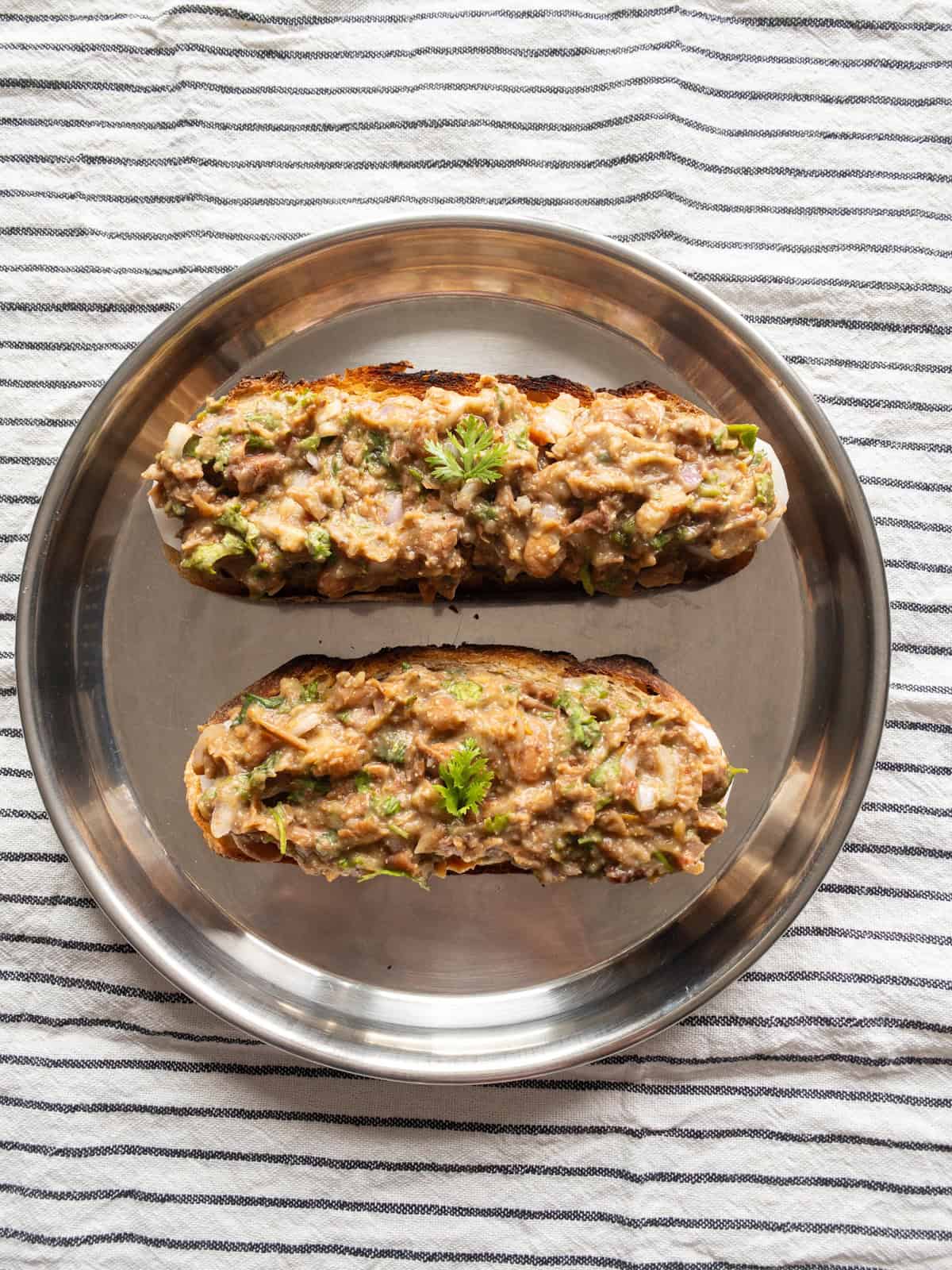 Two toasted bread slices topped with cucumber and mashed kidney bean mixture on a steel plate.