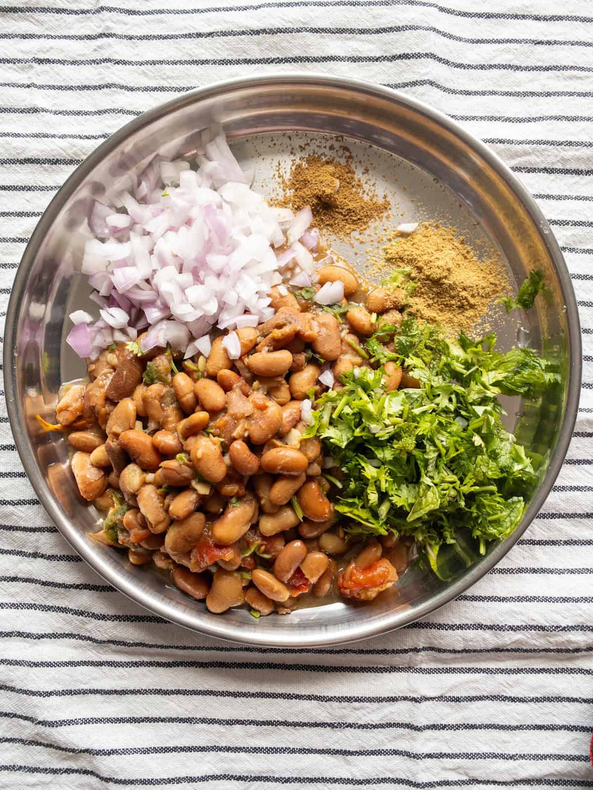 Boiled kidney beans, chopped onion, cilantro, mint, and spices arranged in a steel plate.