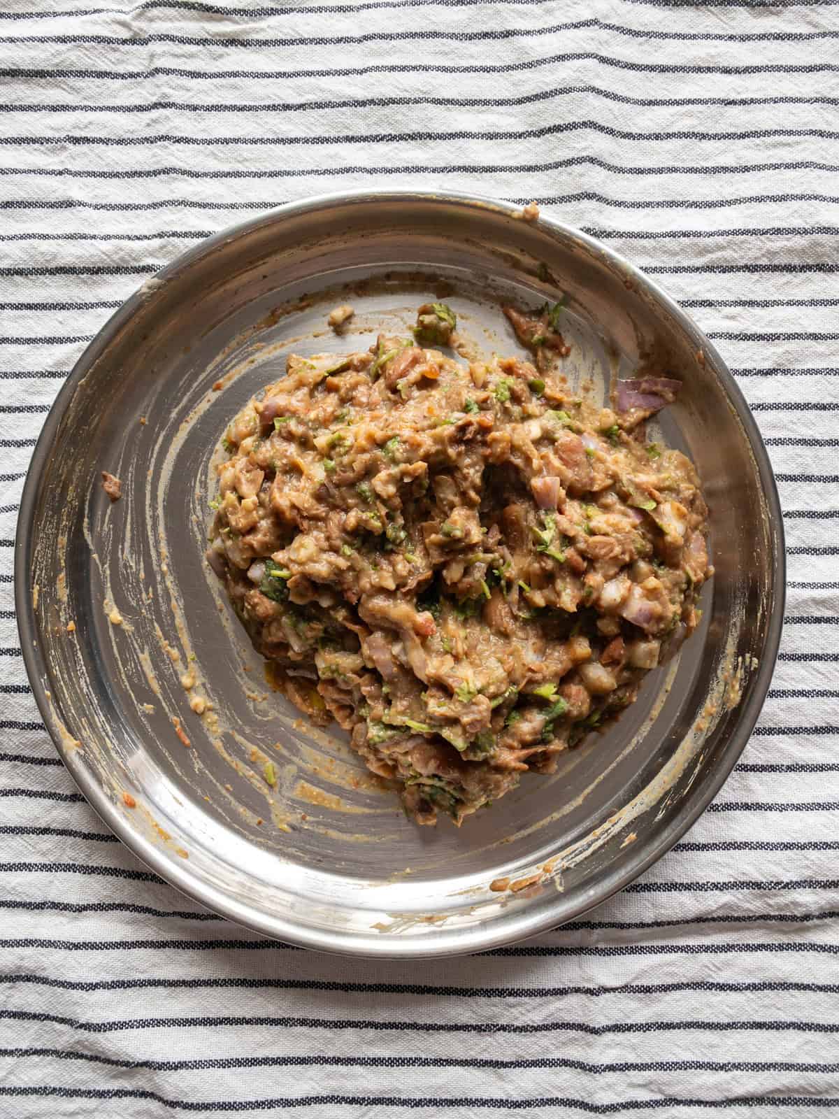 Mashed kidney bean mixture with onions, herbs, and spices in a steel plate.