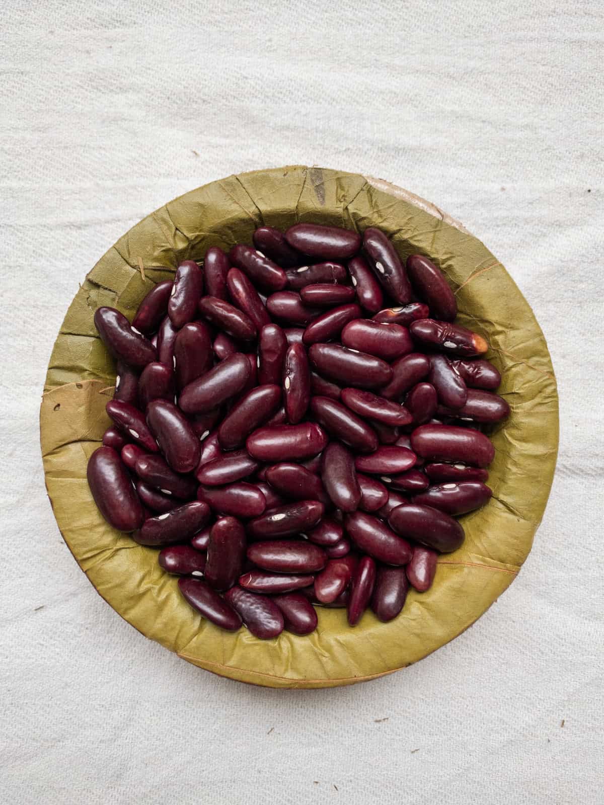 Red kidney beans in a leaf bowl on a white cloth.