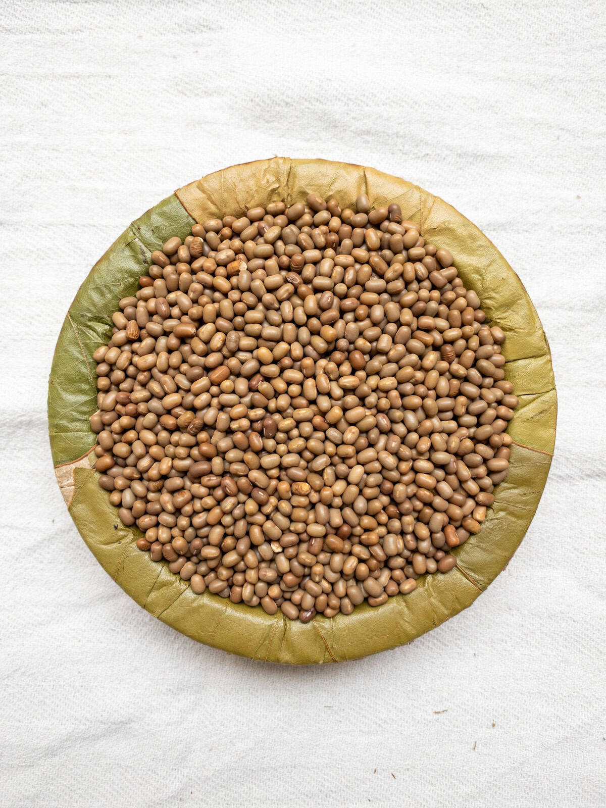 Moth beans in a leaf bowl on a white cloth.