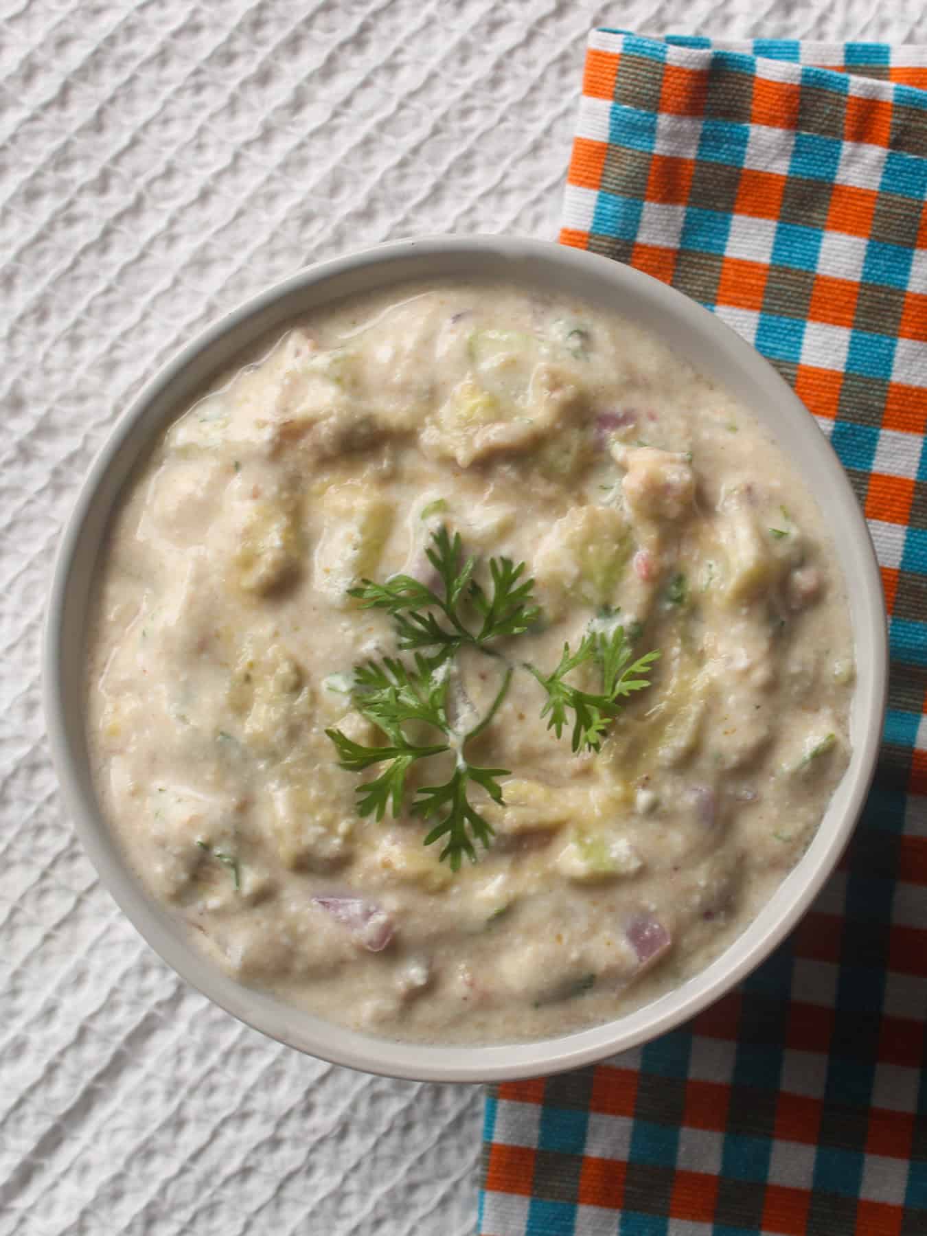 Creamy avocado raita with cucumber and onion in a white bowl, topped with fresh coriander.