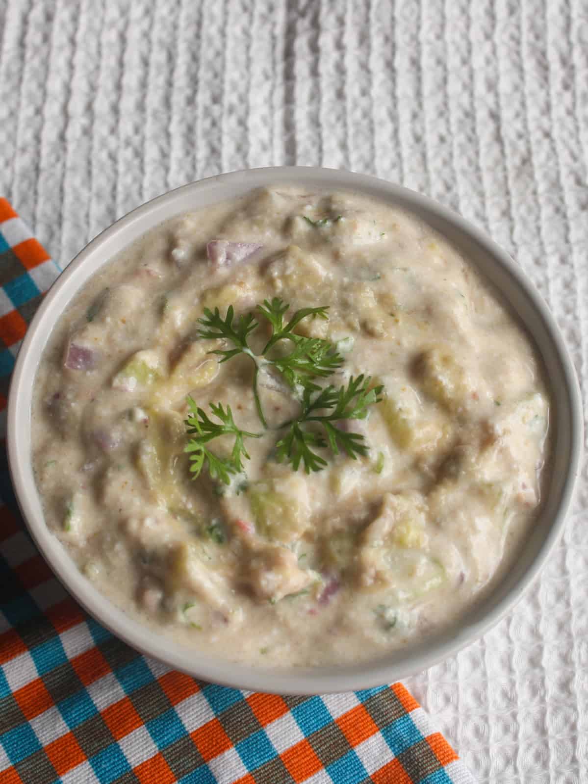 Thick avocado yogurt dip with visible cucumber and onion pieces and fresh coriander on top.