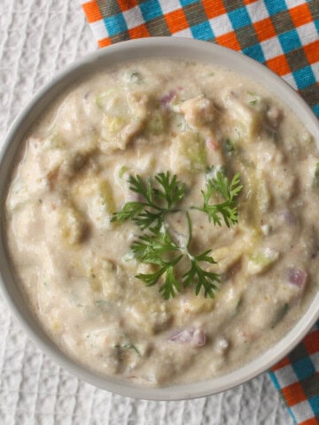 Finished creamy avocado raita in a white bowl with fresh coriander arranged in the center.