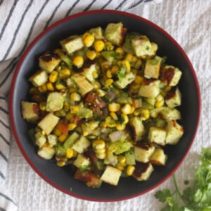 Overhead serving of corn paneer chaat salad with seared paneer cubes, corn, cucumber, tomato, onion, and fresh coriander.