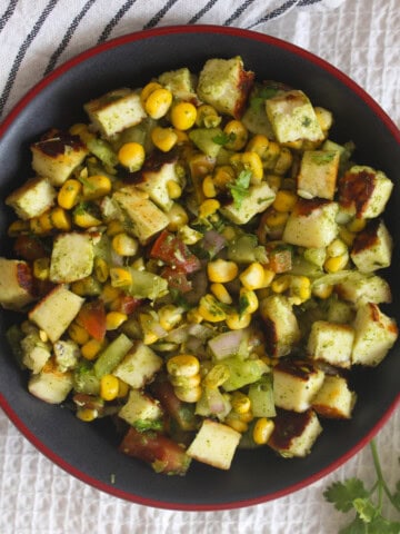 Overhead serving of corn paneer chaat salad with seared paneer cubes, corn, cucumber, tomato, onion, and fresh coriander.