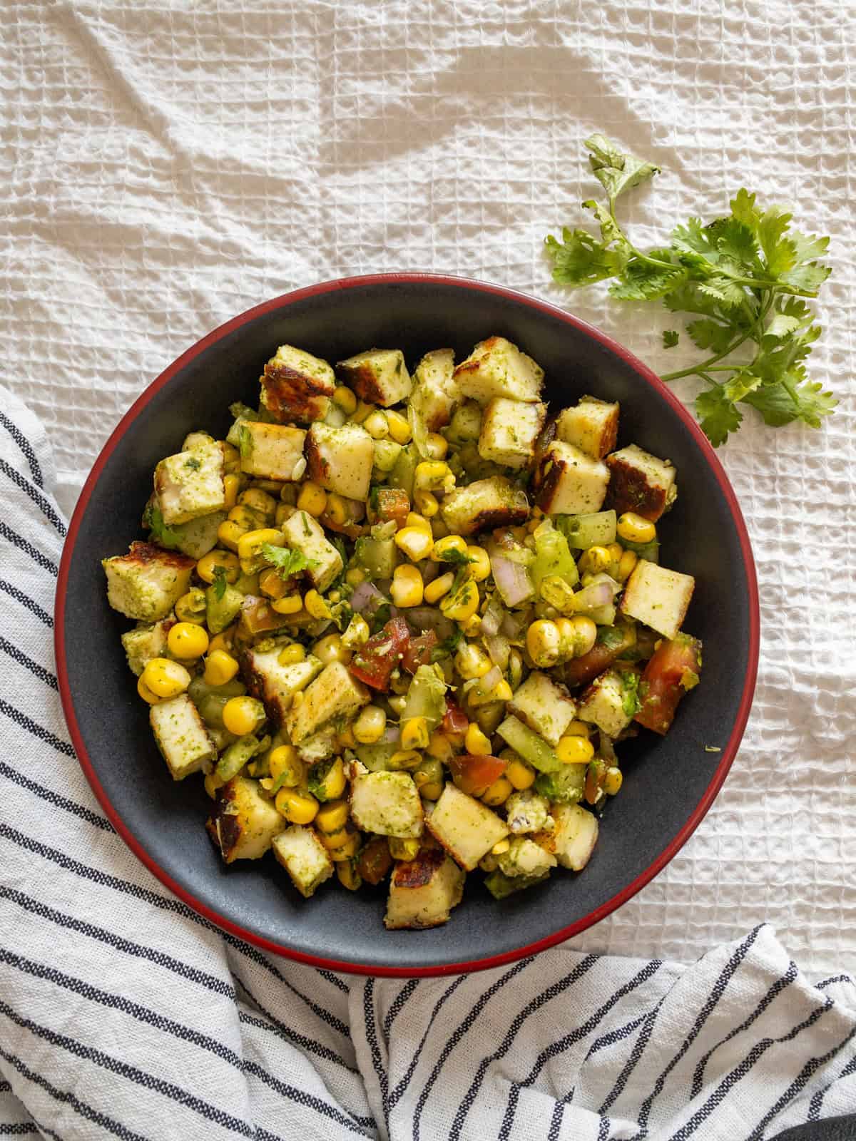 Corn paneer chaat salad served in a black and red bowl with browned paneer, sweet corn, fresh vegetables, and coriander.