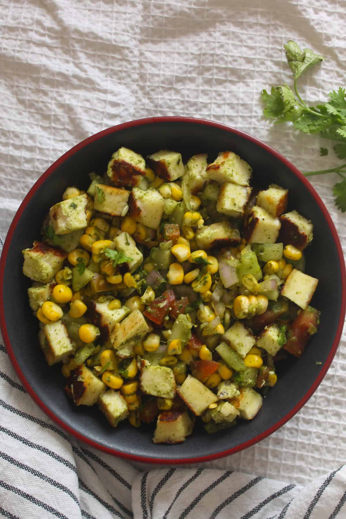 Corn paneer chaat salad with golden paneer cubes, sweet corn, cucumber, tomato, onion, and coriander served in a dark bowl.