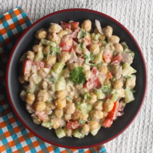 Creamy chickpea salad with cucumber, tomato, onion, and coriander served in a black bowl with a red rim.