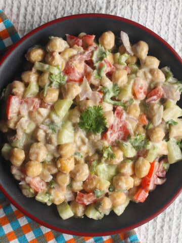 Creamy chickpea salad with cucumber, tomato, onion, and coriander served in a black bowl with a red rim.