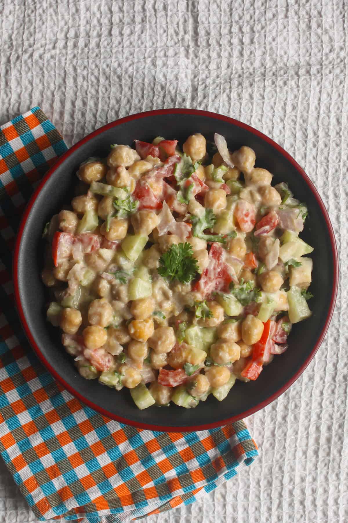 Creamy chickpea salad with visible chickpeas, cucumber, tomato, onion, and coriander served in a black bowl.