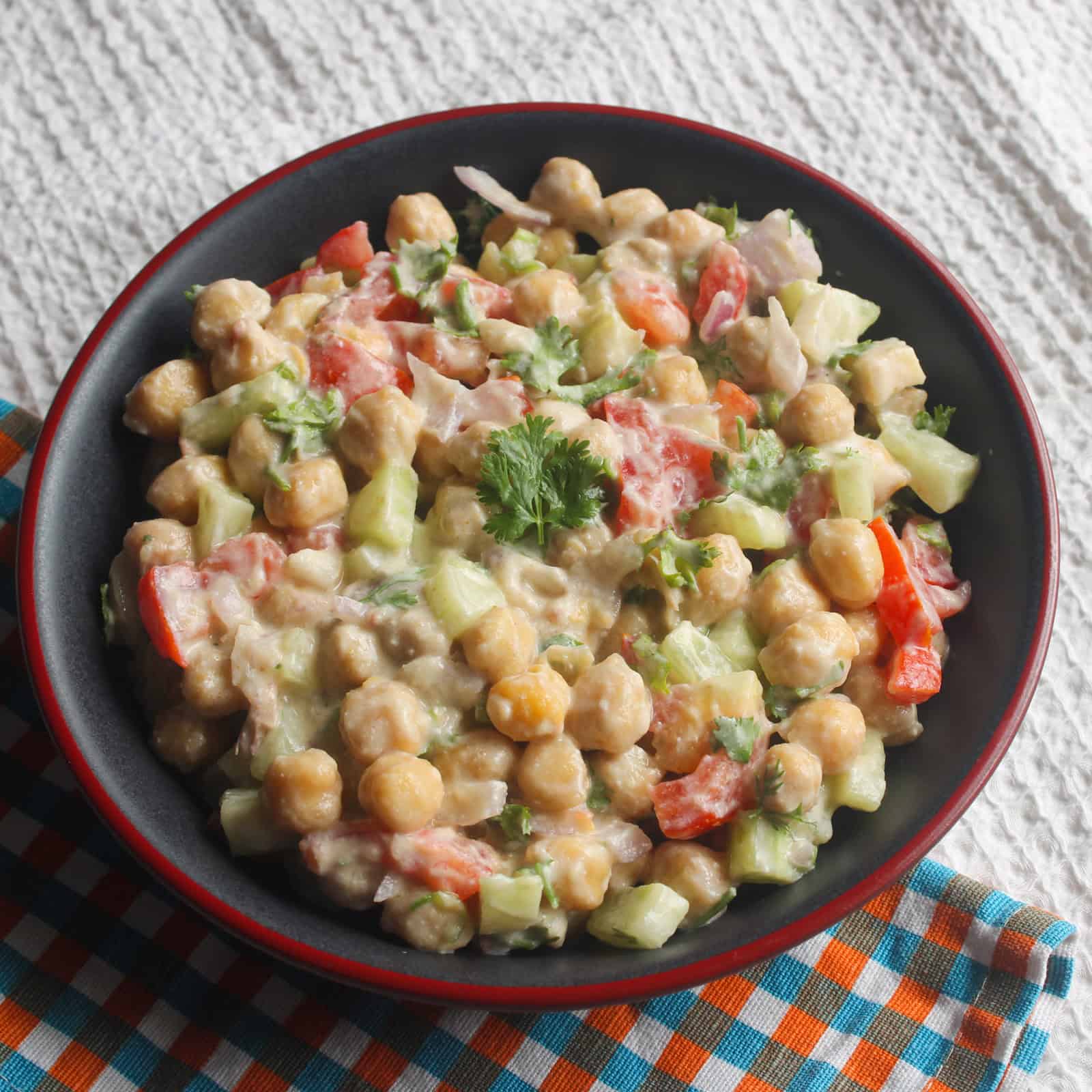 Close serving view of creamy chickpea salad with chickpeas, cucumber, tomato, onion, and fresh coriander.