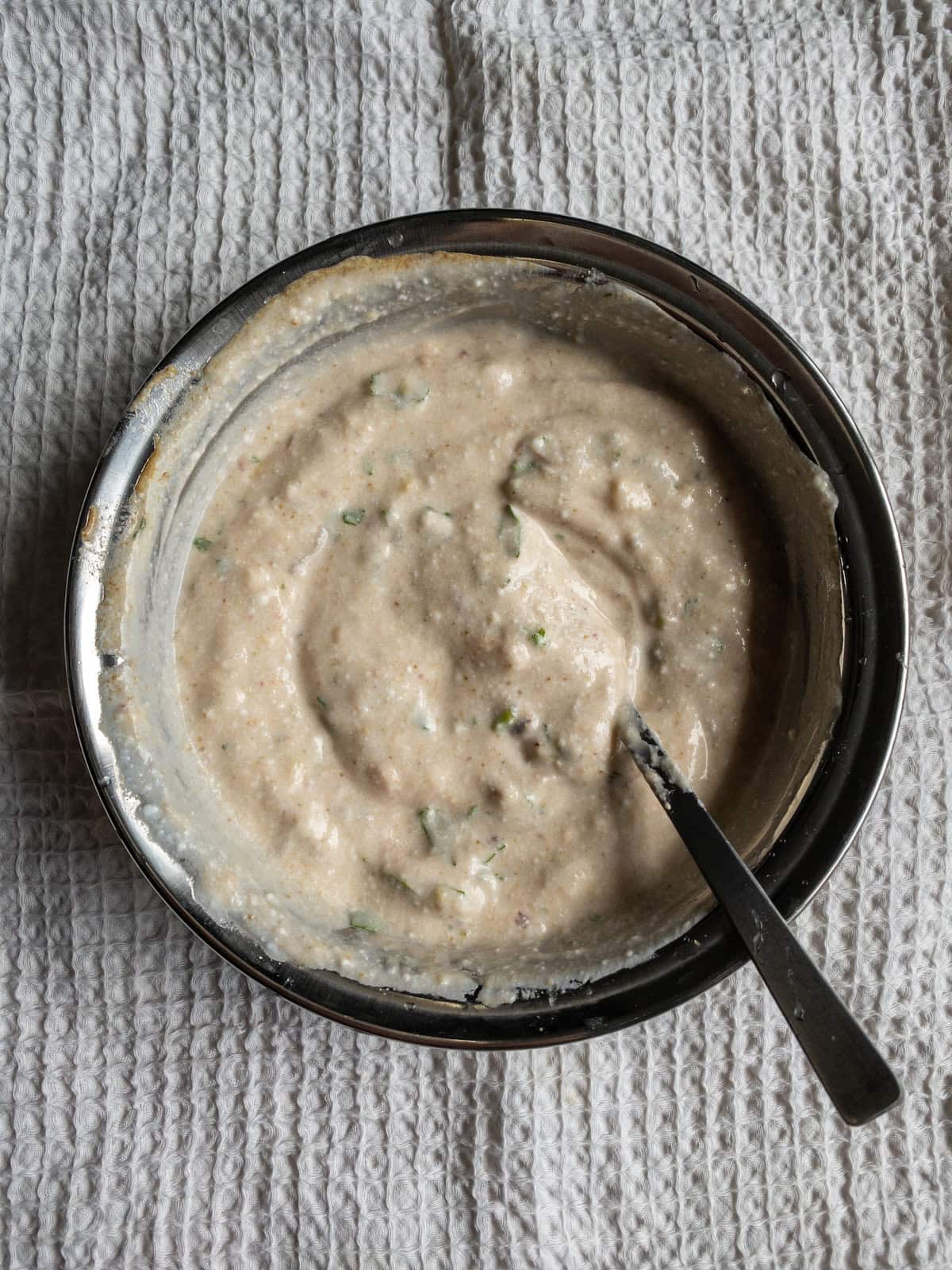 Creamy avocado yogurt dressing mixed in a steel bowl with small pieces of coriander visible.