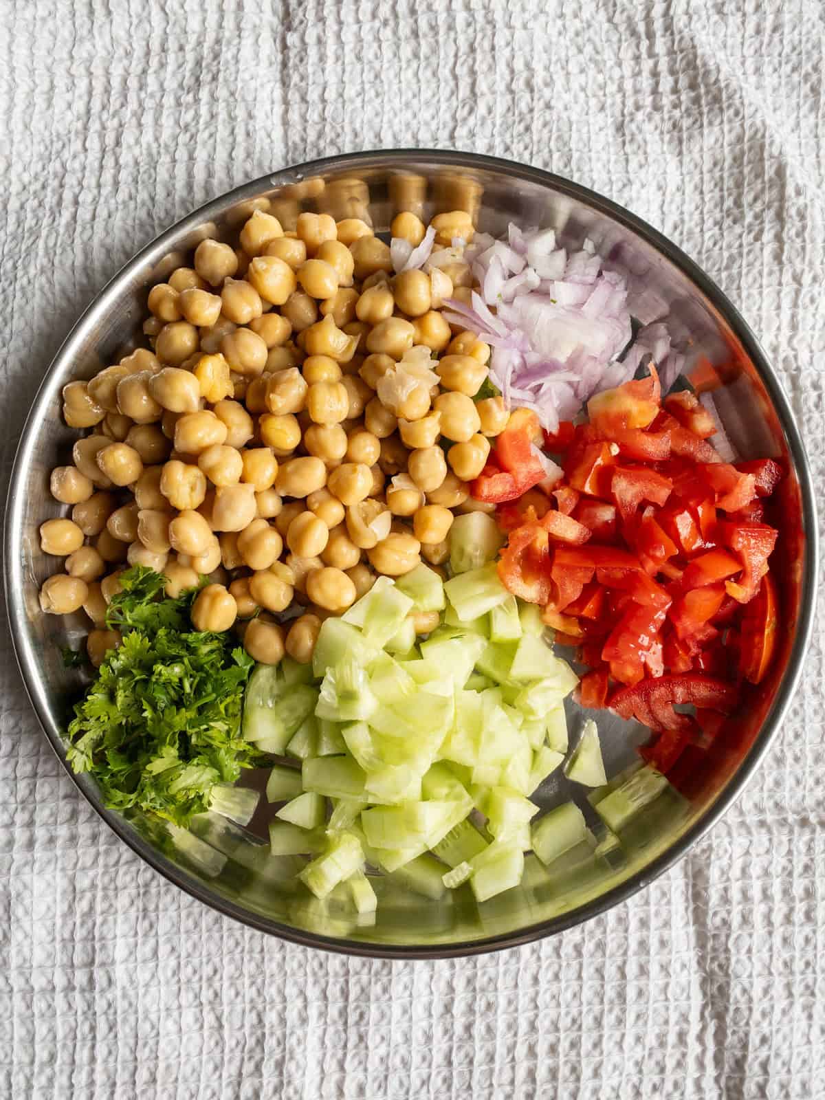 Cooked chickpeas with chopped cucumber, tomato, onion, and fresh coriander arranged on a steel plate.