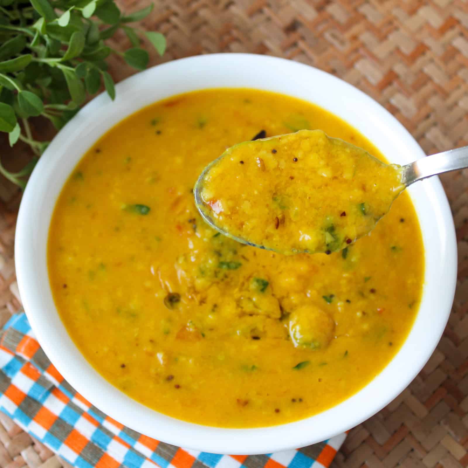Creamy fenugreek toor dal served in a white bowl with a spoonful lifted above it.