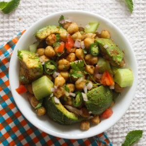 Close overhead view of Indian avocado chickpea salad with creamy avocado, chickpeas, cucumber, tomato, onion, and coriander.