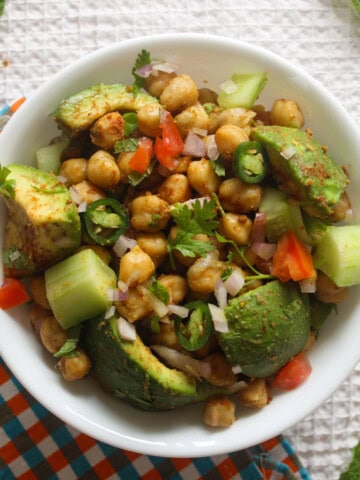 Close overhead view of Indian avocado chickpea salad with creamy avocado, chickpeas, cucumber, tomato, onion, and coriander.