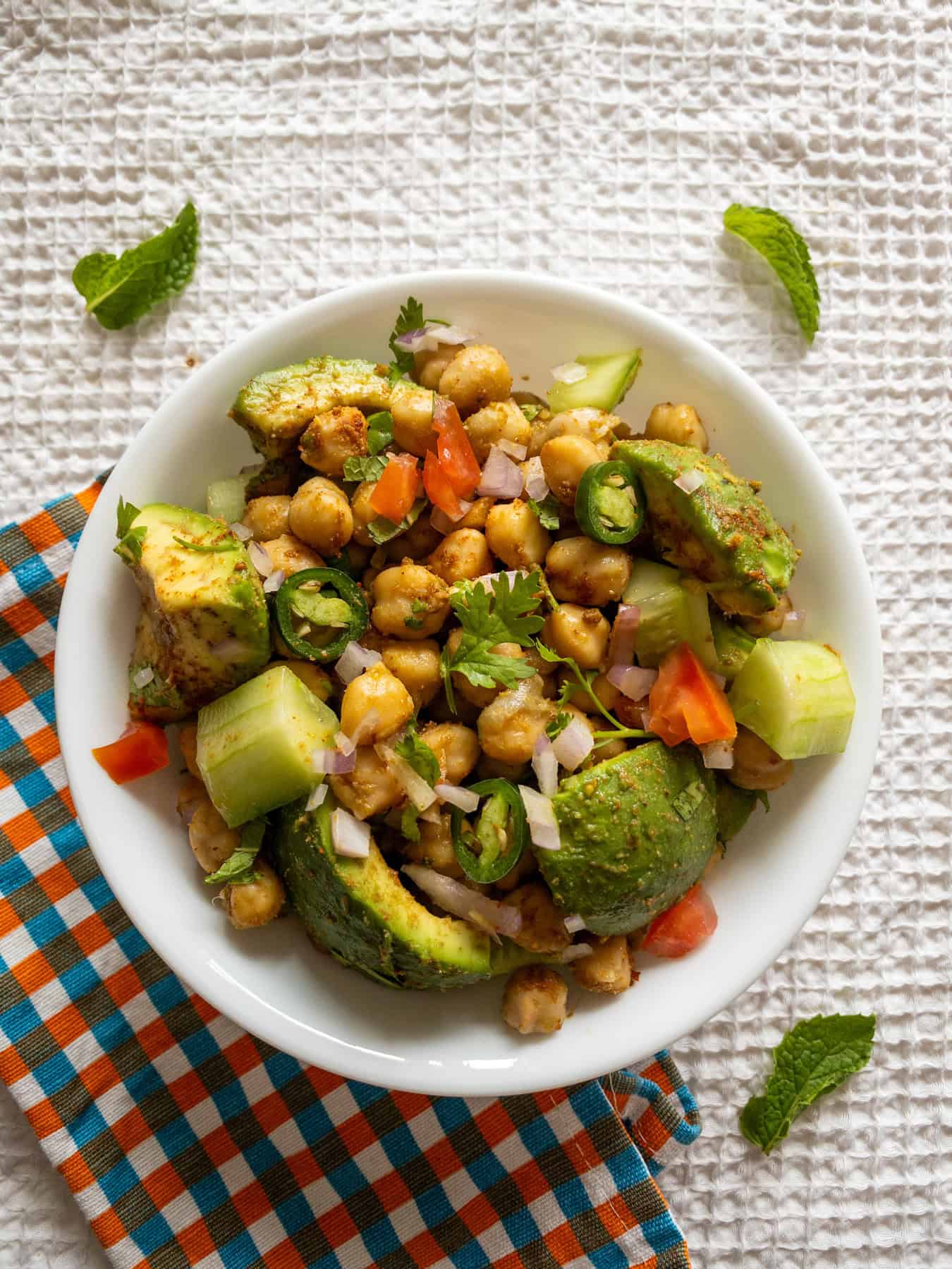 Overhead view of Indian avocado chickpea salad with avocado chunks, chickpeas, cucumber, tomato, onion, and fresh coriander.