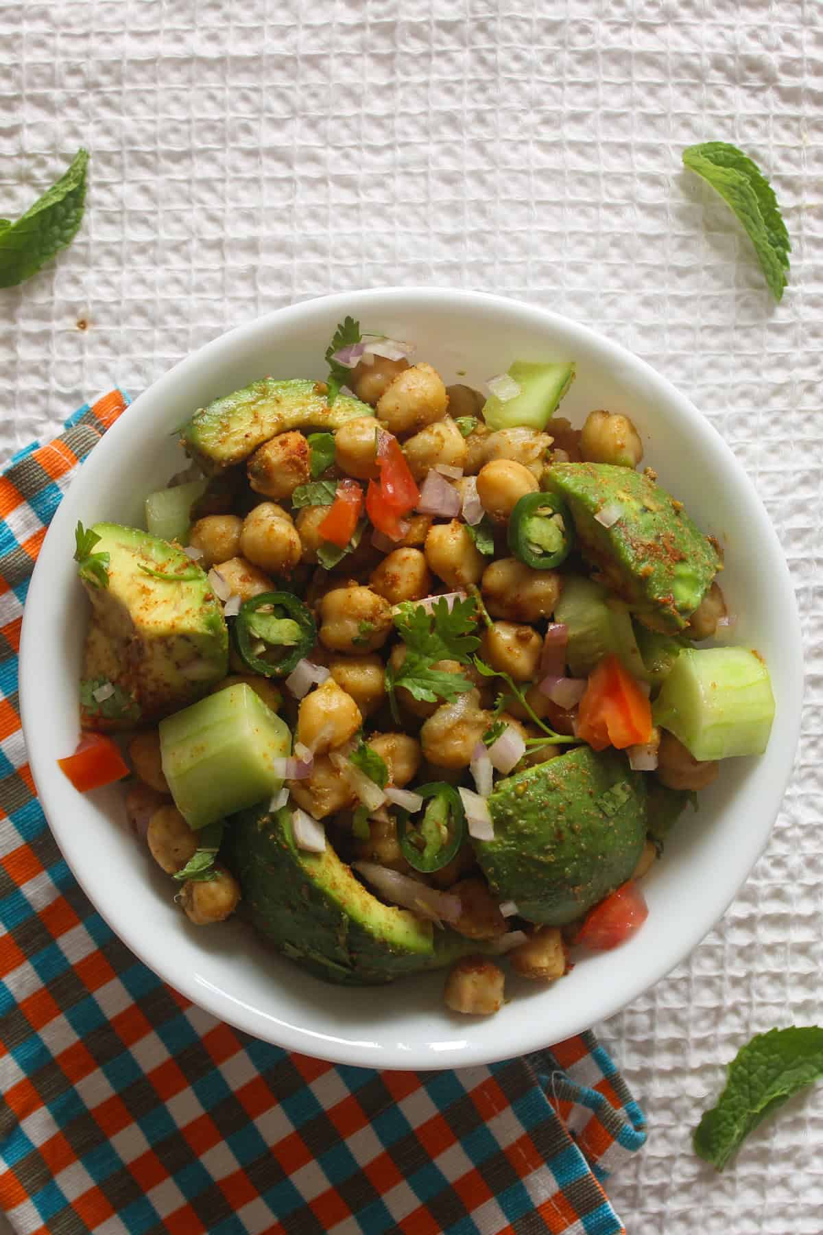 Finished Indian avocado chickpea salad with avocado chunks, chickpeas, cucumber, tomato, onion, and coriander in a white bowl.