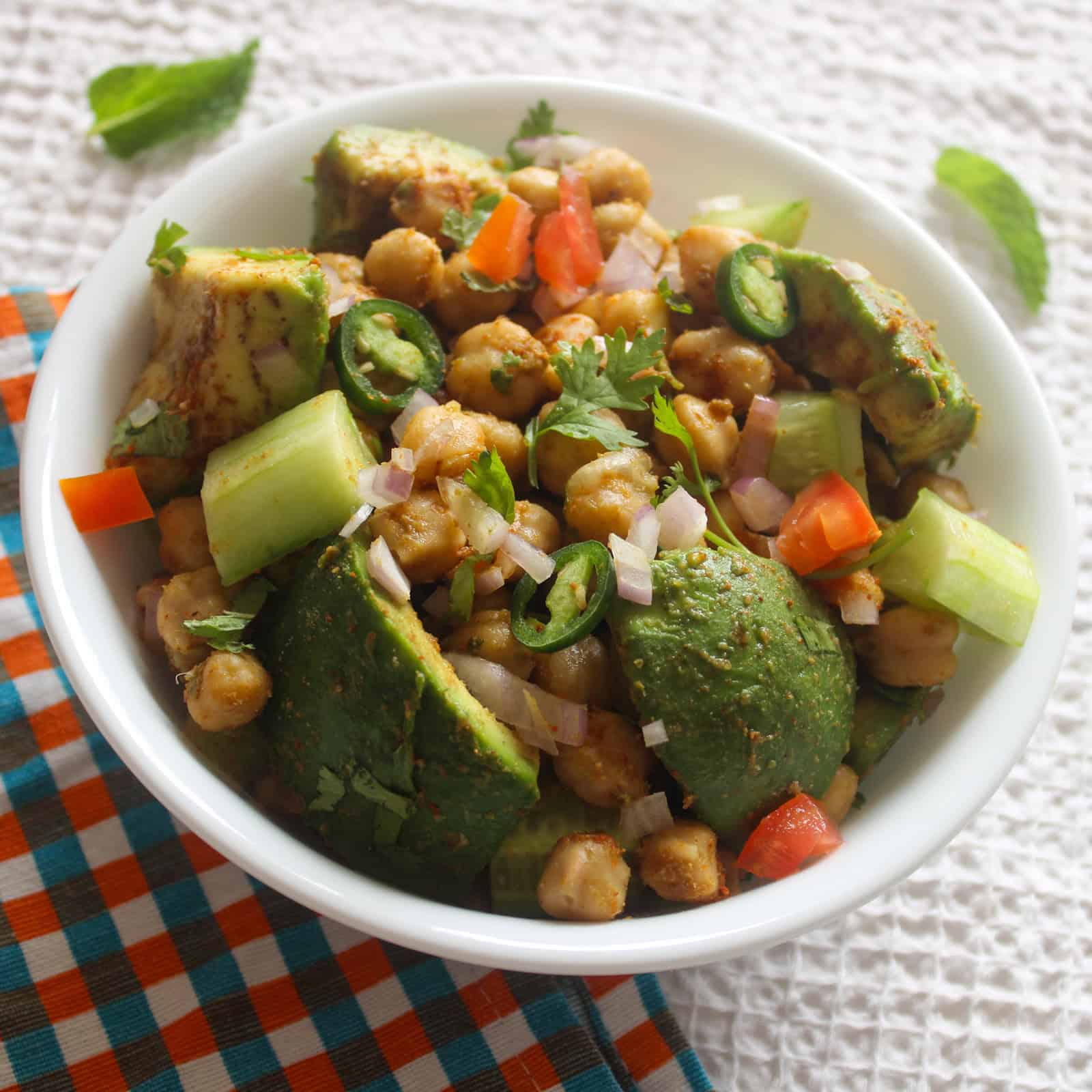 Indian avocado chickpea salad with avocado, chickpeas, cucumber, tomato, onion, and coriander served in a white bowl.