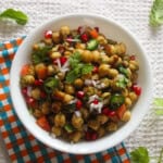 Chickpea chaat salad in a white bowl topped with pomegranate, chopped onion, cilantro, mint, tomato, and sliced green chili.