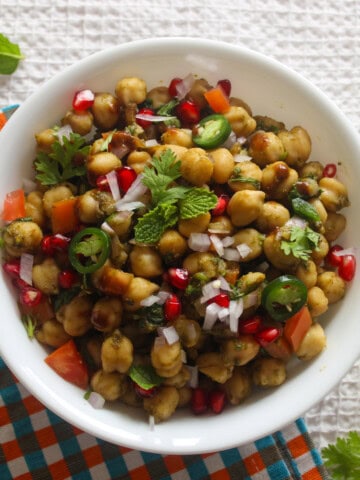 Chickpea chaat salad in a white bowl topped with pomegranate, chopped onion, cilantro, mint, tomato, and sliced green chili.