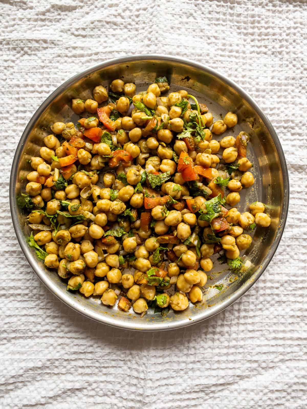 Chickpea chaat salad mixed with tomato, onion, cilantro, mint, chutneys, and spices on a steel plate.